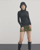 Woman wearing a black minimalist mini skirt that falls mid-thigh, standing confidently. The skirt has a simple, yet elegant design with clean lines and no visible embellishments. She pairs the skirt with a tucked-in white blouse and black pumps for a sophisticated look