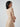 Woman wearing a ribbed cream midi dress with a minimalist design, standing in Australia. The dress falls just below the knee and fits closely to her body, accentuating her figure. She accessorizes with simple jewelry and wears her hair in a sleek and understated style